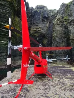 Red Robinson helicopter landed beside towering sea cliffs