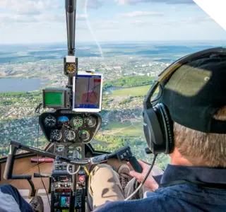 Pilot flying a Robinson helicopter over the countryside