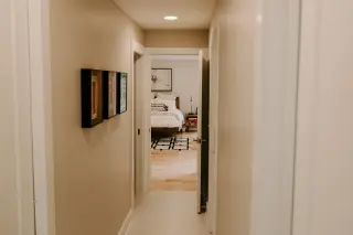 A hallway leading to a bedroom with a bed, nightstand, and wall art.