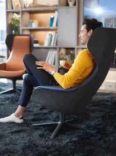 Mann entspannt mit Kaffeetasse in ergonomischem Sessel in gemütlicher Büro-Lounge