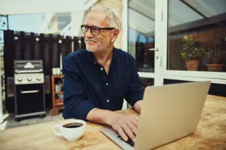 Smiling senior man drinking coffee and using