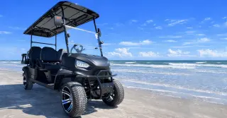 A rugged black ATV parked on a sandy beach under a blue sky.