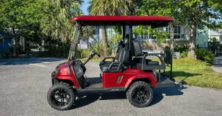 Red golf cart parked outdoors on a sunny day.