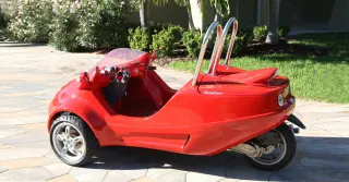A bright red, vintage three-wheeled vehicle with handlebars and an open cockpit.