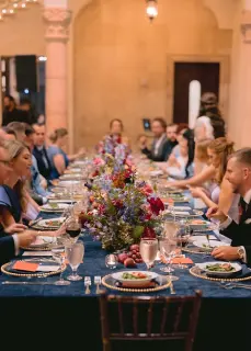 People seated at a long dinner table with floral centerpieces