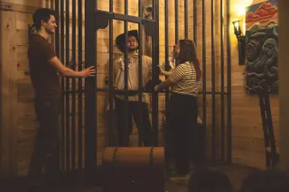 Drie mensen in een escape room, één in een grote gevangeniscel en twee buiten de cel die met haar praten.