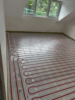 Fußbodenheizung mit roten Heizrohren auf Metallträgerplatten im Dachgeschoss