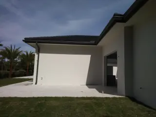 Dark bronze seamless gutters and downspout on a modern white stucco home with palms