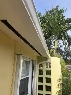 White gutter and downspout on a yellow stucco home with palm trees