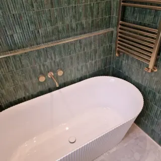 A finished bathroom with a freestanding bath and green fluted tiles