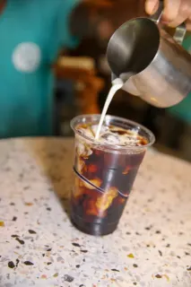 Pouring cream into an iced coffee.