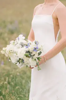 A woman in a white wedding dress holding a bouquet of white and purple flowers.