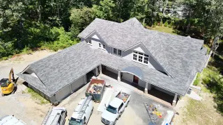 Newly installed gray shingle roof on modern house with landscaped surroundings, featuring construction vehicles and materials in the driveway, highlighting Mac Exterior Solutions' roofing services.