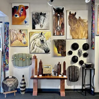 Art gallery display featuring paintings of horses and other animals, decorative objects, and sculptures, with spot lighting overhead.