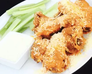 The image is showing our Spicy Garlic Parmesan Wings with celery and ranch dressing.