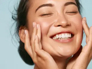 Woman embraces her cheeks with clear skin and a smile on her face.