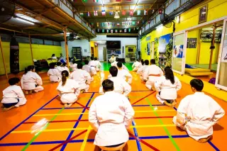 นักเรียน IMAC Dojo ในชุดฝึกสีขาวนั่งเซซะบนเบาะ หันหน้าเข้าหาครูในโดโจลาดพร้าว 101